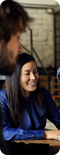 Een vrouw in een blauwe blouse glimlacht tijdens een gesprek aan tafel met collega’s in een modern kantoor.