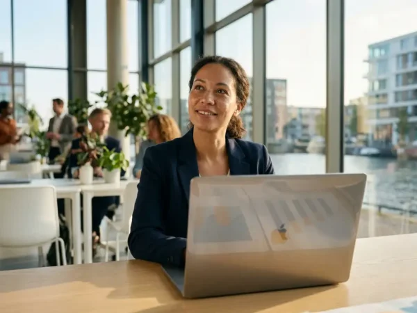 Professional werkt op laptop in modern Nederlands kantoor met natuurlijk licht en datavisualisaties op scherm.