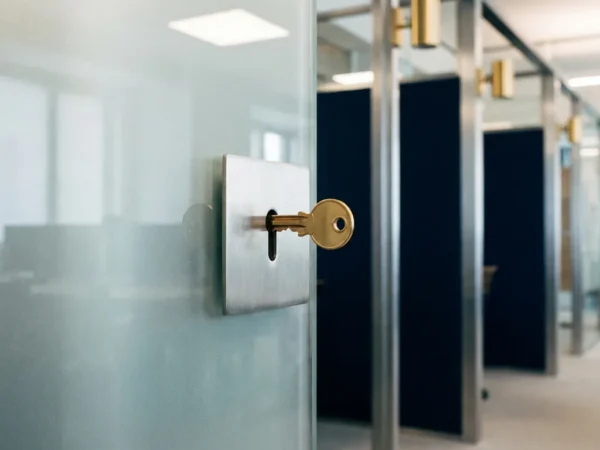 Messing sleutel in modern sleutelgat van matglazen paneel, met kantoorgang op de achtergrond en warme messing accenten.